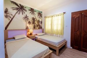 two beds in a room with palm trees on the wall at Segara Sadhu Inn Kuta by ecommerceloka in Kuta