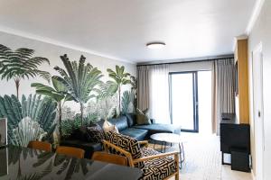 a living room with a blue couch and palm trees mural at Santos Seaview Apartment in Mossel Bay
