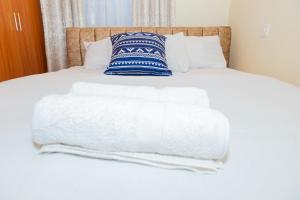 ein Bett mit weißer Bettwäsche und einem blauen und weißen Kissen in der Unterkunft The Stay Comfort in Nyeri