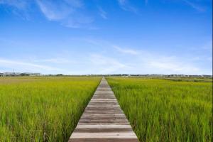 a wooden pathway through a field of green grass at Folly Vacation Vintage Cottage with Stunning Views 218 in Folly Beach
