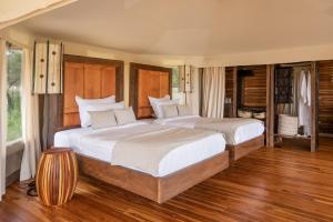 two beds in a bedroom with wood floors and windows at Aurari Camp in Serengeti