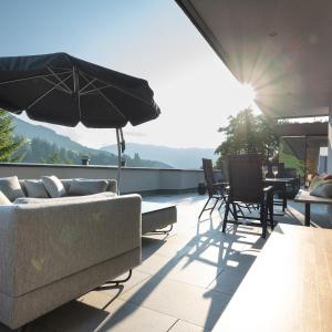 eine Terrasse mit einem Sofa, Stühlen und einem Sonnenschirm in der Unterkunft Bergleben Maria Alm - Haus Panorama in Maria Alm am Steinernen Meer