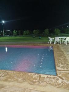 uma piscina à noite com mesas e cadeiras brancas em Villa atlas farm strictement pour les familles em Marrakech