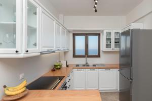 a kitchen with white cabinets and a stainless steel refrigerator at Luxury Villa Noesis with Pool and Seaview in Roussospítion