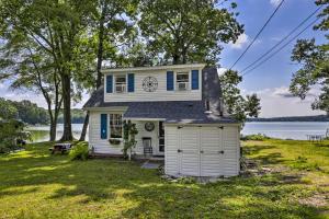a small white house with a garage in front of a lake at Lakefront Cottage with Covered Porch and Dock! in Coventry