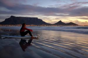 una mujer sentada en una tabla de surf en la playa en Prestigious Guest Villa, en Ciudad del Cabo