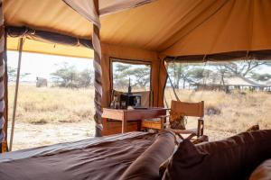 Bett in einem Zelt mit einem Schreibtisch in der Unterkunft Mawe Tented Camp in Serengeti-Savanne
