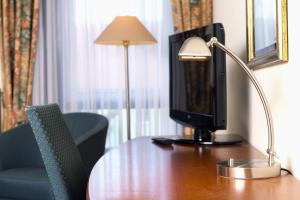 a desk with a monitor and a lamp on a table at Wyndham Garden Hennigsdorf Berlin in Hennigsdorf