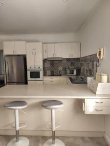 a kitchen with white cabinets and two bar stools at Brom Cottage in Mooloolah