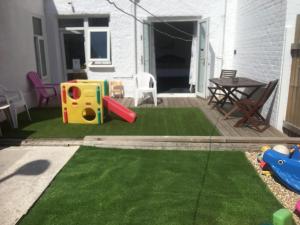 a small backyard with a playground with green grass at BARBIE HOUSE ,OPPOSITE The BEACH & PIER ,2 GROUND FLOOR APARTMENTS each with Private Car space & Garden , Free Access next Door to the Stunning BALLET & MAKE UP SCHOOL & a Beautiful LADYS BEAUTY SALON in Paignton