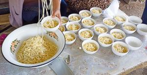 a woman is preparing noodles in white bowls on a table at Karakol Yurt Village in Karakol