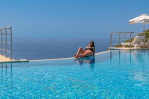 a woman sitting on the edge of a swimming pool at Petani Bay Hotel - Adults Only in Vóvikes