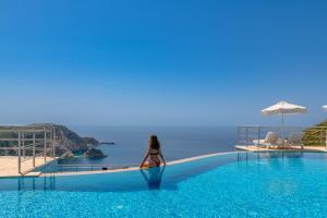 a woman sitting in a swimming pool looking out at the ocean at Petani Bay Hotel - Adults Only in Vóvikes