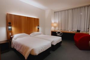 a hotel room with two beds and a red chair at NEW IPOINT HOTEL in San Giovanni in Persiceto