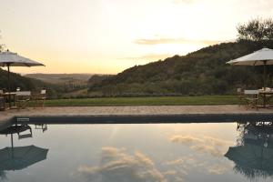 uma piscina de água com mesas e guarda-sóis em Tenuta Santo Pietro em Pienza