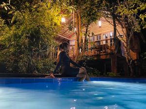 una mujer sentada en el borde de una piscina en Habarana Tree house Mutu village, en Habarana