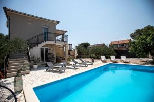 a swimming pool with chairs and a house at Villa Marleku in Pakoštane