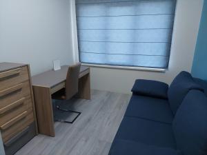 a room with a desk and a blue couch and a window at Apartamentai in Garliava