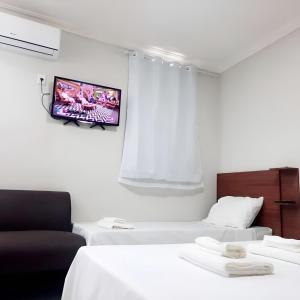 a room with two beds and a tv on the wall at Pousada Avenida in Teixeira de Freitas