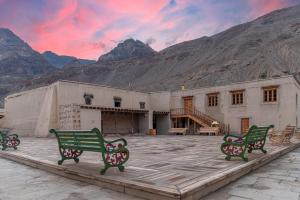 a building with three green benches in front of a mountain at Echor Mud Huts Tabo, Spiti Valley in Kaza