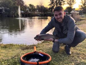 un hombre sosteniendo un pez en una cesta junto a un estanque en Lanseria Country Estate, en Lanseria