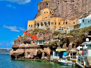 a building on the side of a mountain next to the water at Mermaid Cave Apartment Old Port, Fira in Fira