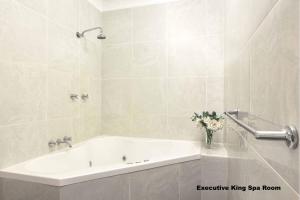 een witte badkamer met een bad en een vaas met bloemen bij Mt Tamborine Stonehaven Boutique Hotel in Mount Tamborine