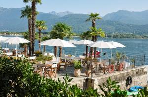 un restaurant avec des tables, des parasols blancs et l'eau dans l'établissement Hotel Carillon, à Baveno