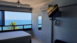 a bedroom with a flat screen tv and a view of the ocean at Farol Barra Flat in Salvador