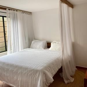 a bedroom with a bed with white sheets and a window at Lilac Hideaway in Karatu