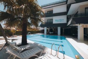 a swimming pool with chairs and a palm tree in front of a building at PALMİLA BUTİK OTEL in Silifke