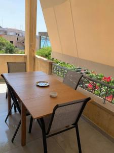 Mimozas Apartment Porto Heli في بورتوخيلي: طاولة وكراسي خشبية على شرفة بها زهور