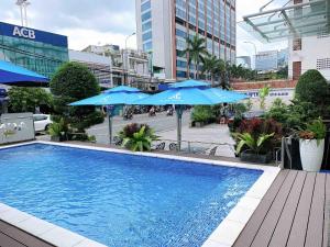 a swimming pool with blue umbrellas on a city street at Acnos Grand Hotel in Ho Chi Minh City