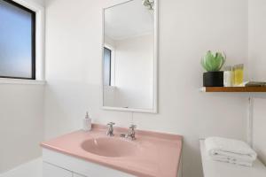 La salle de bains est pourvue d'un lavabo rose et d'un miroir. dans l'établissement Family 3BR Home with Netflix and Fully Fenced Yard, à Auckland