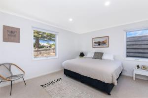 a white bedroom with a bed and a chair at Lyons Cottage - a quaint Whalers Cottage in heart of Port Fairy in Port Fairy