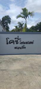 een bord voor een gebouw met een palmboom op de achtergrond bij โคซี่ โฮมสเตย์ in Suan Phung