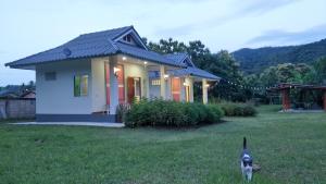 un chien debout dans l'herbe devant une maison dans l'établissement Pimpisa Garden, à Ban Khuang Kom