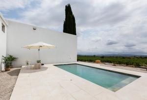 a swimming pool with an umbrella next to a white building at Lidia Rural House in San Martín Sarroca