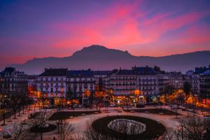 Hôtel d’Angleterre Grenoble Hyper-Centre في غرونوبل: مدينة وقت الغروب مع جبل في الخلفية