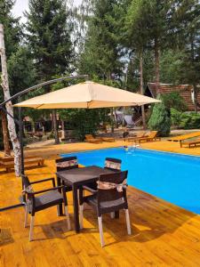 einen Tisch und Stühle unter einem Sonnenschirm neben einem Pool in der Unterkunft "Garaske Breze" Kućice za izdavanje sa bazenom in Aranđelovac