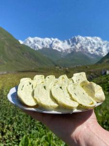 a person holding a plate of food with mountains in the background at Maxvshi in Ushguli