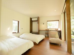 een slaapkamer met 2 bedden en een stoel. bij Coboushi ハナレ in Niseko