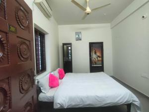 a bedroom with a white bed with pink pillows at Jinnens Tourist Home in Ponnāni