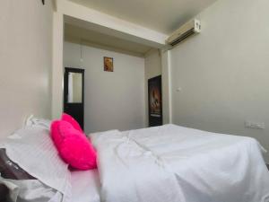 a white bed with a pink pillow on top of it at Jinnens Tourist Home in Ponnāni