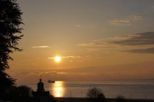 una puesta de sol sobre el agua con un barco en la distancia en Le Manoir des Impressionnistes - Bord de Mer, en Honfleur