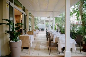 un restaurante con mesas blancas, sillas y plantas en Dépendance Hotel Lalla, en Cesenatico