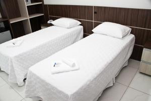 two beds in a hotel room with white sheets at Miotto Executive Hotel in Navegantes