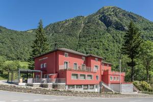 ein rotes Gebäude vor einem Berg in der Unterkunft Relais Lucomagno in Olivone