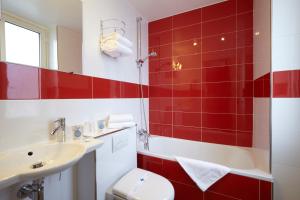 La salle de bains est pourvue de carrelage rouge, de toilettes et d'un lavabo. dans l'établissement Kyriad Paris 10 - Canal Saint Martin - République, à Paris