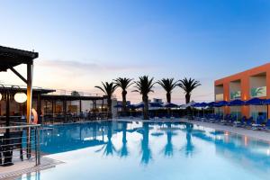 einem großen Pool mit Palmen und einem Gebäude in der Unterkunft Rethymno Village in Platanes